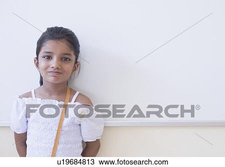 Stock Image - Portrait of a schoolgirl leaning against a whiteboard in a classroom. Fotosearch