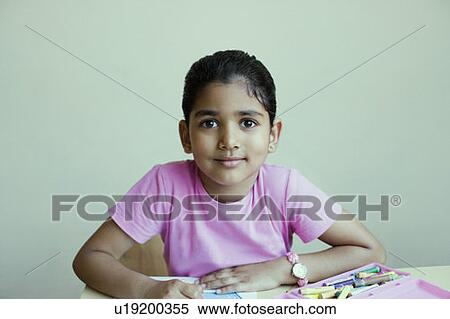 Stock Photography - Portrait of a schoolgirl sitting at a table and drawing with crayons. Fotosearch