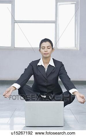 Stock Image - Businesswoman doing yoga in front of a laptop. Fotosearch
