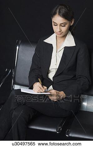 Stock Photography - Businesswoman sitting on a chair and writing on a notebook. Fotosearch