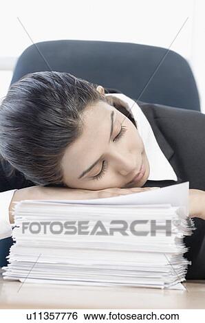 Stock Photograph - Close-up of a businesswoman leaning on a stack of papers and sleeping. Fotosearch