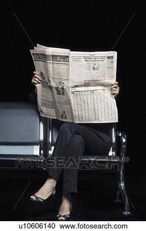 Stock Image - Low section view of a businesswoman sitting on a bench and reading a newspaper. Fotosearch