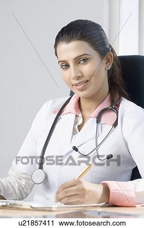 Stock Image - Portrait of a female doctor sitting on a chair and holding a pen. Fotosearch