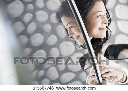 Stock Photograph - Close-up of a young woman peeking through a car window. Fotosearch