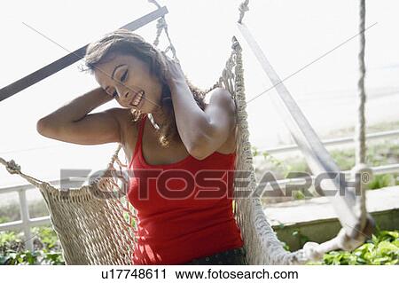 Stock Image - Close-up of a young woman sitting in a hammock and smiling. Fotosearch