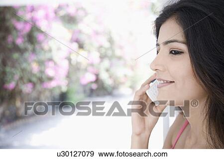 Stock Photo - Close-up of a young woman talking on a mobile phone and smiling. Fotosearch