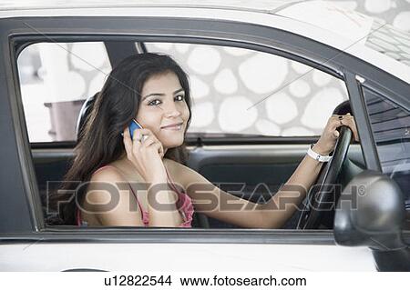 Portrait of a young woman sitting inside a car and talking on a mobile phone View Large Photo Image Picture - Portrait of a young woman sitting inside a car and talking on a mobile phone. Fotosearch