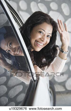 Stock Photograph - Portrait of a young woman waving her hand from a window of a car. Fotosearch