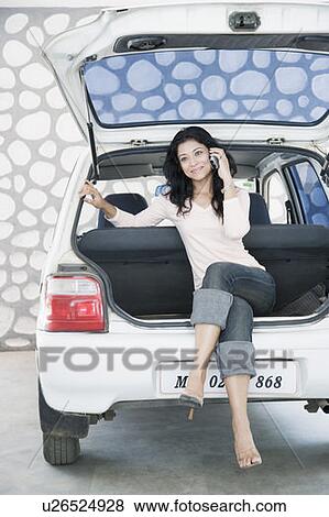Stock Photo - Young woman sitting in a car trunk and talking on a mobile phone. Fotosearch
