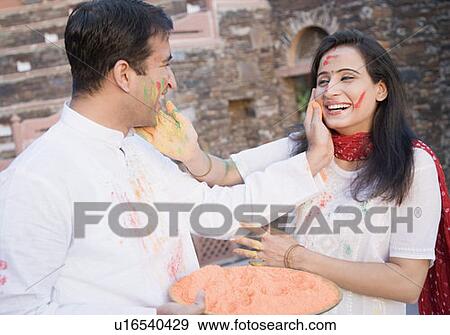 Stock Photo - Close-up of a mid adult couple applying powder paint on each other's face. Fotosearch