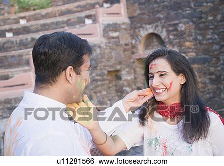 Stock Photograph - Close-up of a mid adult couple applying powder paint on each other's face. Fotosearch