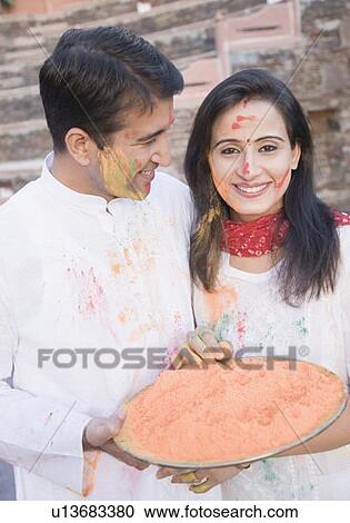 Stock Image - Close-up of a mid adult couple holding a plate of powder paint and smiling. Fotosearch