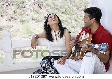 Mid adult man playing a guitar with a mid adult woman sitting beside him and laughing View Large Photo Image Stock Photo - Mid adult man playing a guitar with a mid adult woman sitting beside him and laughing. Fotosearch