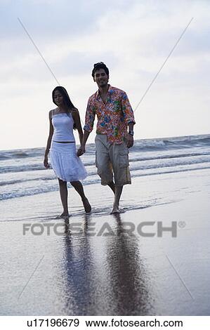 Portrait of a young man holding hands of a young woman and walking on the beach View Large Photo Image Stock Photo - Portrait of a young man holding hands of a young woman and walking on the beach. Fotosearch