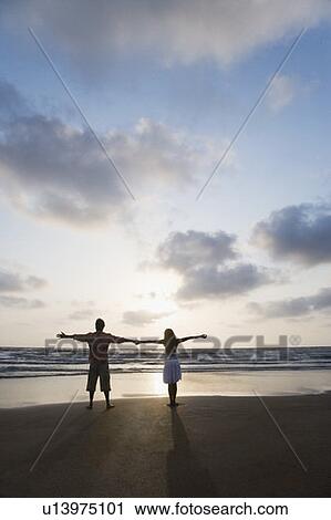 Rear view of a couple standing with their arms outstretched on the beach View Large Photo Image Stock Image - Rear view of a couple standing with their arms outstretched on the beach. Fotosearch