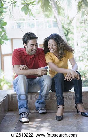 Young man sitting with a young woman and text messaging on a mobile phone View Large Photo Image Stock Image - Young man sitting with a young woman and text messaging on a mobile phone. Fotosearch