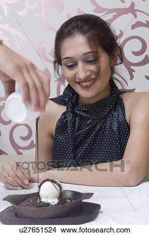 Picture - Close-up of a person's hand pouring choko over the ice-cream in front of a young woman. Fotosearch