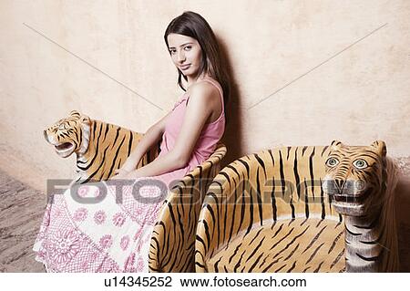 Stock Image - Portrait of a young woman sitting on a chair and grinning. Fotosearch