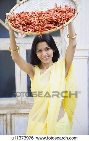 Stock Photograph - Portrait of a young woman spraying red chili peppers from a tray. Fotosearch
