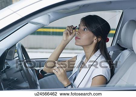 Stock Image - Side profile of a businesswoman applying mascara on her eyes. Fotosearch