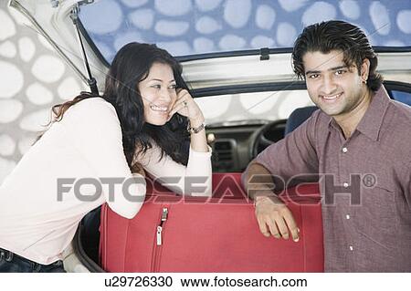 Stock Image - Young couple smiling together in the boot of a car. Fotosearch