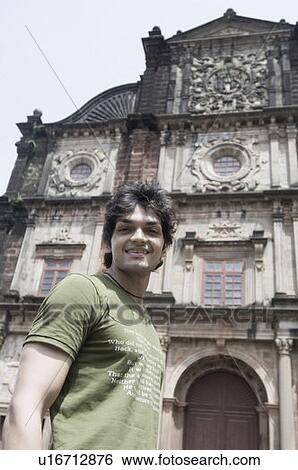 Stock Photograph - Portrait of a young man smiling in front of a building, Goa, India. Fotosearch