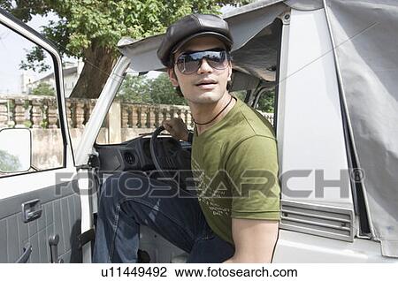 Stock Image - Side profile of a young man sitting in a jeep, Goa, India. Fotosearch