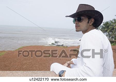 Stock Image - Side profile of a young man sitting on a ledge. Fotosearch