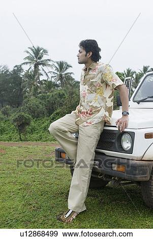Stock Photo - Young man leaning against a car and looking sad. Fotosearch