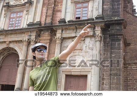 Young man standing in front of a building and pointing, Goa, India View Large Photo Image Stock Image - Young man standing in front of a building and pointing, Goa, India. Fotosearch