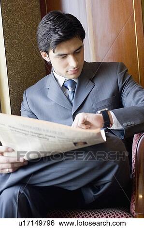 Stock Photograph - Businessman holding a newspaper and checking the time. Fotosearch