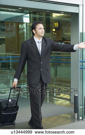 Businessman pulling luggage and hailing a taxi at an airport View Large Photo Image Stock Photo - Businessman pulling luggage and hailing a taxi at an airport. Fotosearch