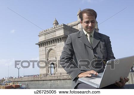 Businessman using a laptop with a monument in the background, Gateway of India, Mumbai, Maharashtra, India View Large Photo Image Stock Photography - Businessman using a laptop with a monument in the background, Gateway of India, Mumbai, Maharashtra, India. Fotosearch