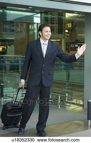 Stock Image - Businessman waving his hands and smiling at an airport. Fotosearch