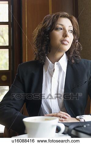 Businesswoman sitting at a table and looking away View Large Photo Image Stock Photograph - Businesswoman sitting at a table and looking away. Fotosearch