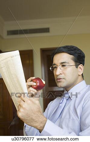 Close-up of a businessman reading a newspaper and eating an apple View Large Photo Image Stock Photo - Close-up of a businessman reading a newspaper and eating an apple. Fotosearch