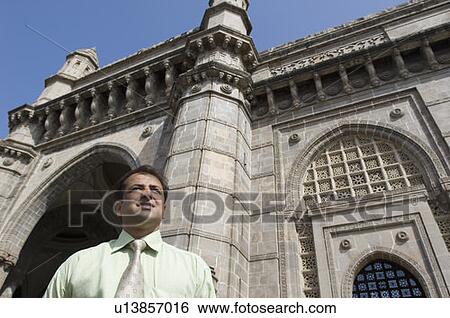 Stock Photograph - Low angle view of a businessman in front of a monument, Gateway of India, Mumbai, Maharashtra, India. Fotosearch