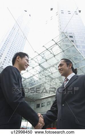 Low angle view of two businessmen shaking hands and smiling, Singapore View Large Photo Image Stock Image - Low angle view of two businessmen shaking hands and smiling, Singapore. Fotosearch