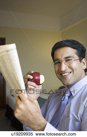 Portrait of a businessman holding a newspaper and eating an apple View Large Photo Image Stock Photography - Portrait of a businessman holding a newspaper and eating an apple. Fotosearch