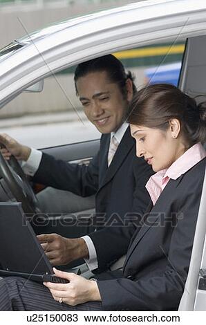 Side profile of a businesswoman using a laptop in a car with a businessman sitting beside her and smiling, Singapore View Large Photo Image Stock Image - Side profile of a businesswoman using a laptop in a car with a businessman sitting beside her and smiling, Singapore. Fotosearch