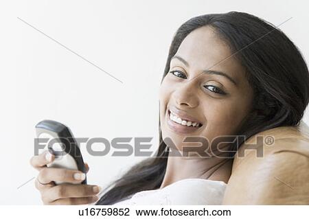 Stock Image - Portrait of a young woman holding a mobile phone and smiling. Fotosearch