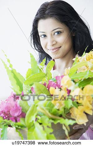 Stock Photo - Portrait of a young woman holding a flower vase and smiling. Fotosearch