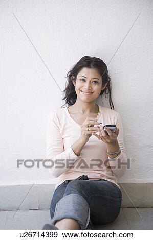Portrait of a young woman leaning against a wall and operating a mobile phone View Large Photo Image Stock Photo - Portrait of a young woman leaning against a wall and operating a mobile phone. Fotosearch