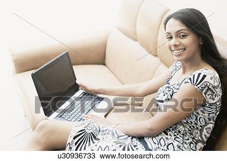 Portrait of a young woman sitting on a couch and using a laptop View Large Photo Image Stock Image - Portrait of a young woman sitting on a couch and using a laptop. Fotosearch