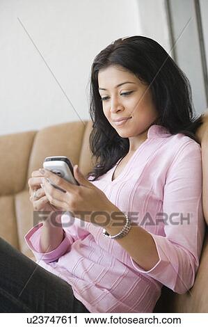 Side profile of a young woman sitting on a couch and operating a mobile phone View Large Photo Image Stock Image - Side profile of a young woman sitting on a couch and operating a mobile phone. Fotosearch