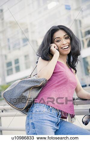 Young woman leaning against a railing and talking on a mobile phone View Large Photo Image Stock Image - Young woman leaning against a railing and talking on a mobile phone. Fotosearch