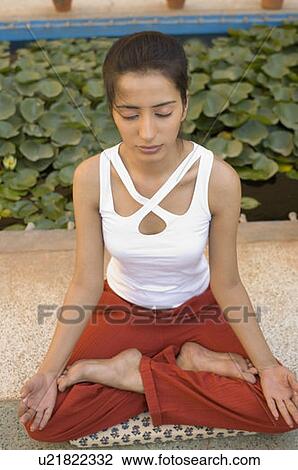 Stock Image - High angle view of a young woman sitting in a lotus position on an exercise mat. Fotosearch