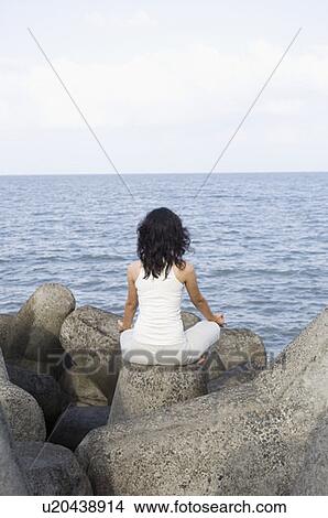 Picture - Rear view of a young woman doing yoga on rocks . Fotosearch