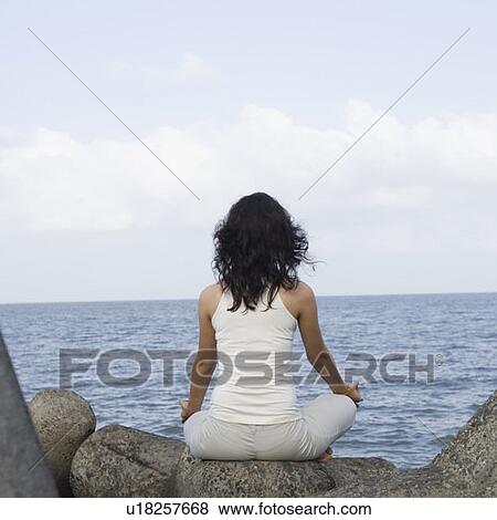 Stock Photo - Rear view of a young woman doing yoga on rocks . Fotosearch
