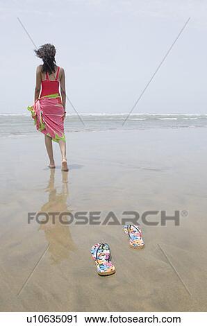 Stock Image - Rear view of a young woman walking on the beach. Fotosearch